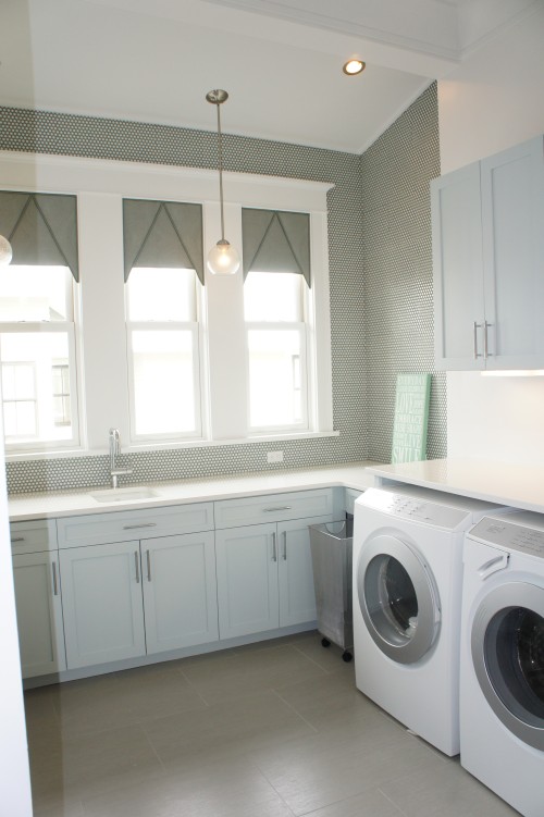 Laundry rooms usually get the cold shoulder in most houses I encounter, but this one is definitely different!  The walls are treated with penny round Ann Sacks tiles with slight gray-blue rims.  The slight color creates a gray color contrast for the walls that looks great against the white trim and pale gray cabinets.  Accent pendant lights add to the charm.  This is the perfect little coastal modern laundry room!